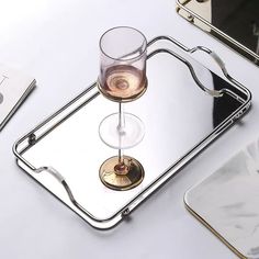 a wine glass sitting on top of a metal tray next to a cell phone and tabletop