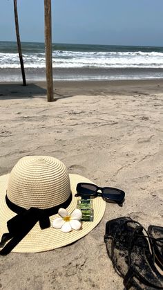 a hat, sunglasses and flip flops lay on the sand at the beach near the ocean