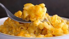 a fork full of macaroni and cheese is being held up by a white bowl