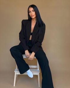 a woman sitting on top of a white chair wearing a black blazer and pants