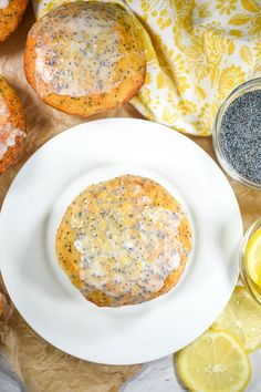 a white plate topped with a muffin next to lemons and poppy seed seeds