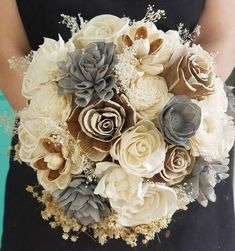 a woman holding a bouquet of white and grey flowers in her hands with the bride's hand