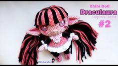 a crocheted doll with pink and black hair wearing a dress, sitting on top of a white surface