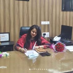 a woman sitting at a desk writing on a piece of paper with flowers in front of her