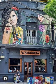 a woman walking down the street in front of a building with murals on it's side