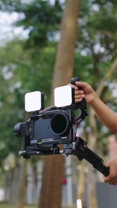 a person holding a video camera in their hand with trees in the backgroud