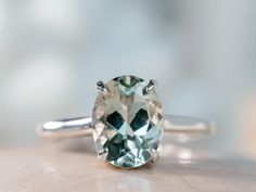 an oval cut green and white diamond ring on top of a table with blurry background