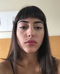 a woman with long dark hair wearing a bra and nose piercings is looking at the camera