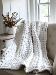 a white crocheted blanket sitting on top of a couch next to a window