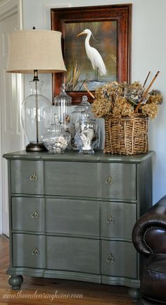 an antique dresser with glass jars and vases on it, next to a lamp