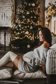 a pregnant woman sitting on a couch in front of a christmas tree