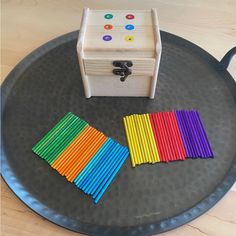 a wooden box sitting on top of a metal tray filled with colored sticks and rainbows