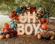 a sign that says oh boy surrounded by balloons and pumpkins in front of some trees