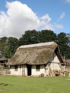 an old thatched roof house with grass and trees in the background