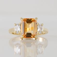 an orange and white diamond ring with three diamonds on the side, set in yellow gold