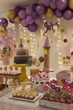 a table topped with lots of cakes and desserts covered in purple and gold balloons