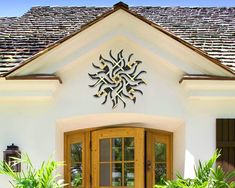 a white house with two wooden doors and plants in the front yard, on a sunny day