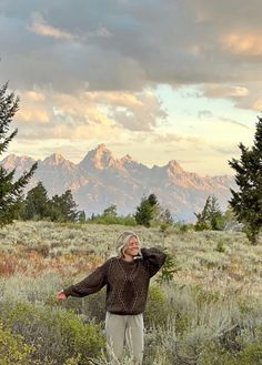 a woman standing in the middle of a field with mountains in the backgroud