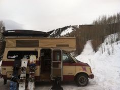 an rv parked on the side of a snow covered hill with skis and snowboards attached to it