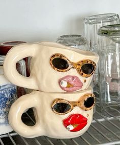 two ceramic mugs with faces painted on them sitting on a shelf in a kitchen