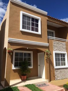 a tan house with white windows and plants