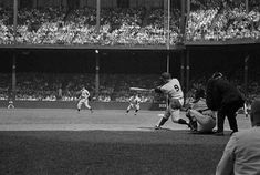 a black and white photo of a baseball player swinging at a ball during a game