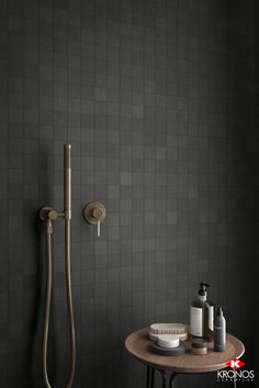 a bathroom with black tile walls and a shower head, soap dispenser, and other items on the table