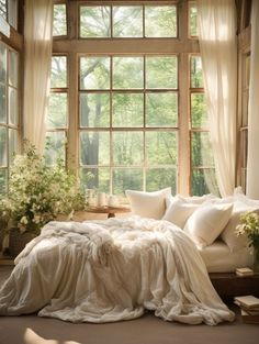 a bed sitting in front of a window covered in white sheets and pillows next to flowers