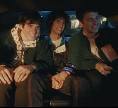 three young men are sitting in the back seat of a car, smiling and laughing