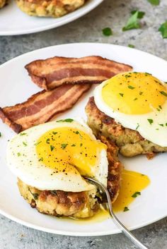 two plates with eggs and bacon on them, one has a fork stuck in it