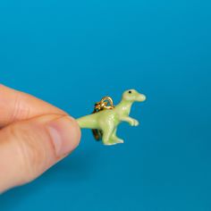 a tiny toy dinosaur is being held by a person's hand on a blue background