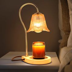 a lit candle is sitting on a table next to a lamp with a glass jar