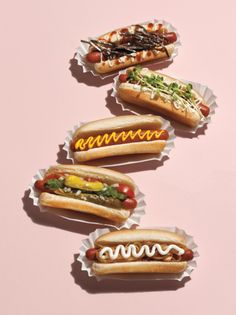 five hotdogs with condiments arranged on pink background