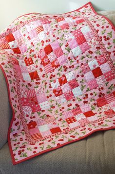 a pink and red quilt sitting on top of a gray couch next to a pillow