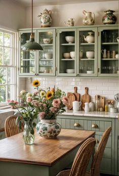 a kitchen filled with lots of green cabinets and flowers in vases on the counter