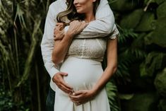 a pregnant couple cuddling in front of green plants