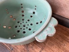 a green bowl with holes in it on a wooden table next to a planter