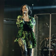 a woman standing on top of a stage with her hands in her pockets and holding a microphone