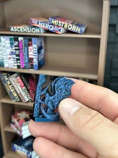 a hand holding a miniature book in front of a bookshelf filled with books