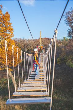 a person walking across a rope bridge in the woods on a sunny day with autumn foliage