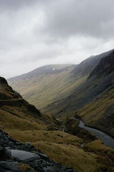 a valley with mountains in the background and a stream running through it on a cloudy day