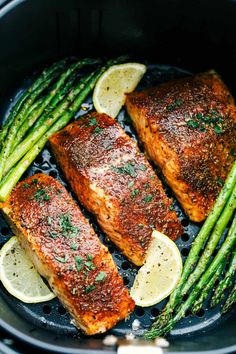 salmon and asparagus in a skillet with lemon wedges