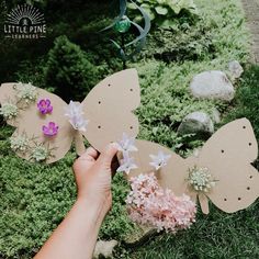 someone is holding some paper butterflies in their hand with flowers on them and moss growing around the wings