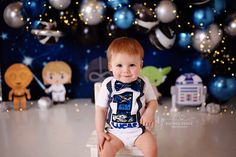 a baby boy sitting on a chair in front of balloons and decorations for his first birthday