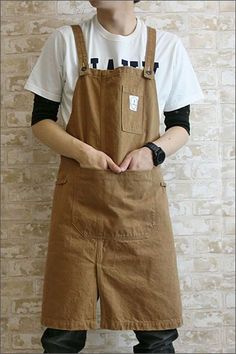 a man standing in front of a brick wall wearing overalls and a white t - shirt