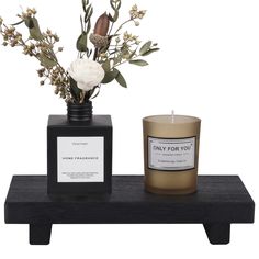 a candle and vase with flowers on a black shelf next to each other in front of a white background