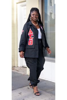 a woman standing on the sidewalk in front of a building wearing a black jacket and pants