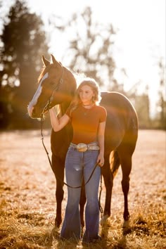 a woman standing next to a brown horse on top of a dry grass covered field