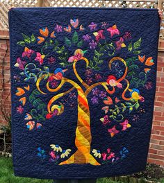 a quilted tree with colorful leaves and flowers on it in front of a fence