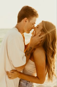 a man and woman standing next to each other on the beach with their arms around each other